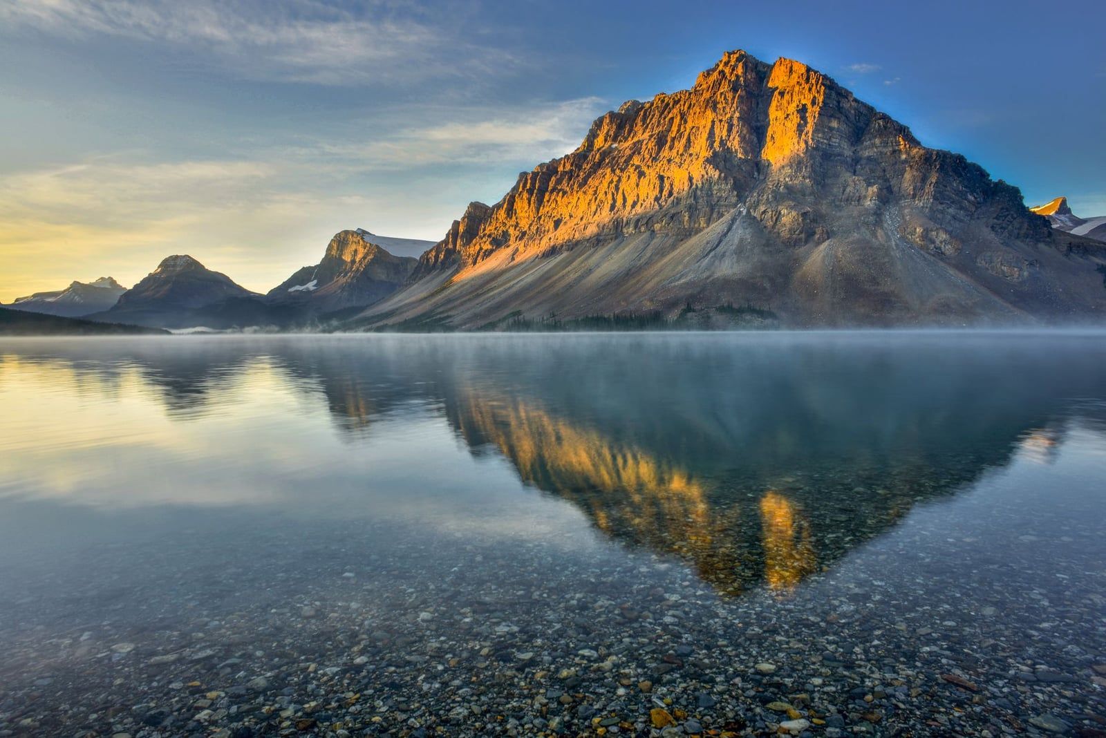 Morgensonne beleuchtet die felsigen Gipfel, die sich im klaren, ruhigen Wasser des Bow Lake entlang der Icefields-Parkway-Route nach Jasper spiegeln.