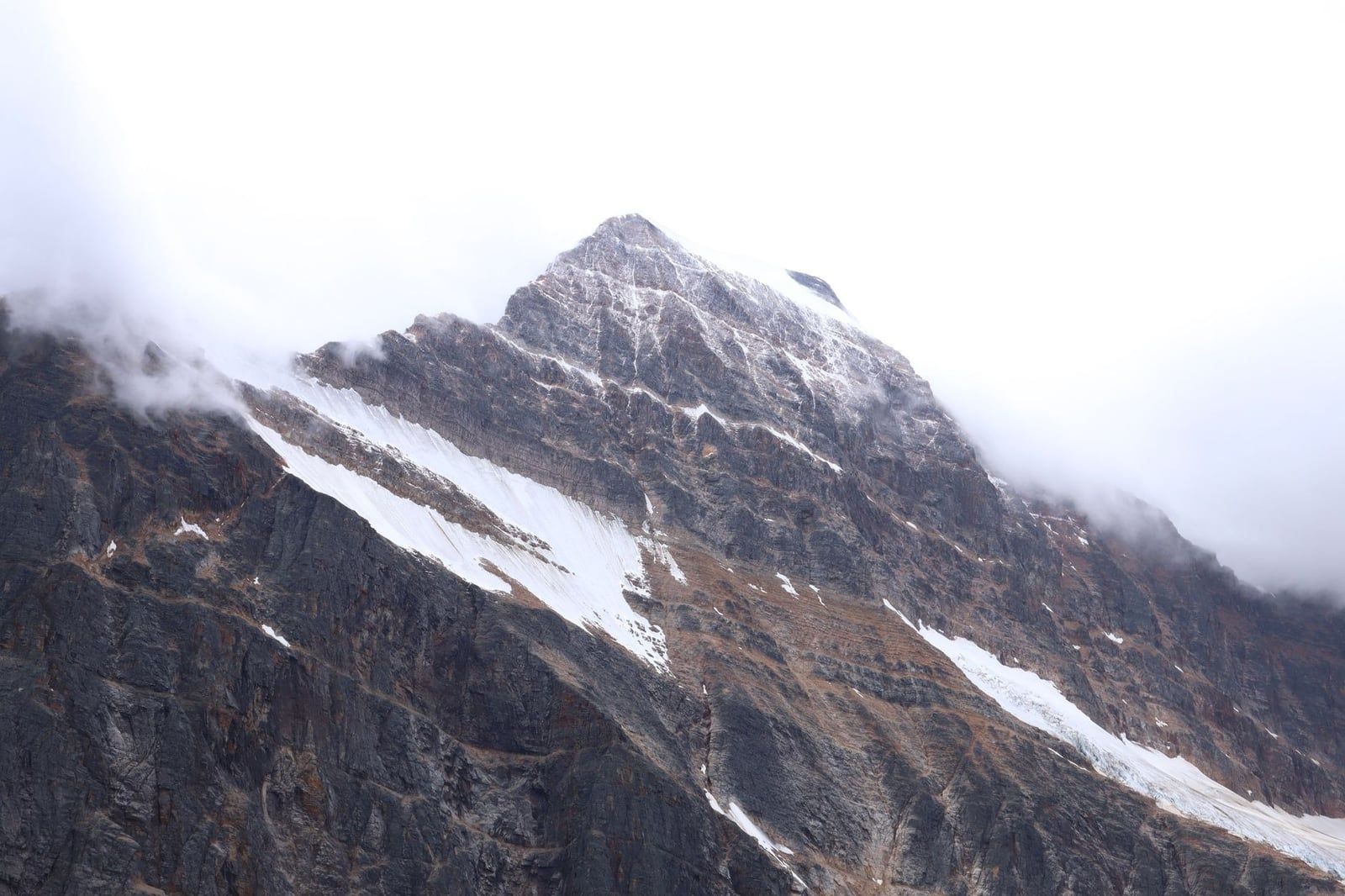 La vetta aspra e punteggiata di neve del Mount Edith Cavell emerge dalle nuvole fitte nel Parco Nazionale Jasper.