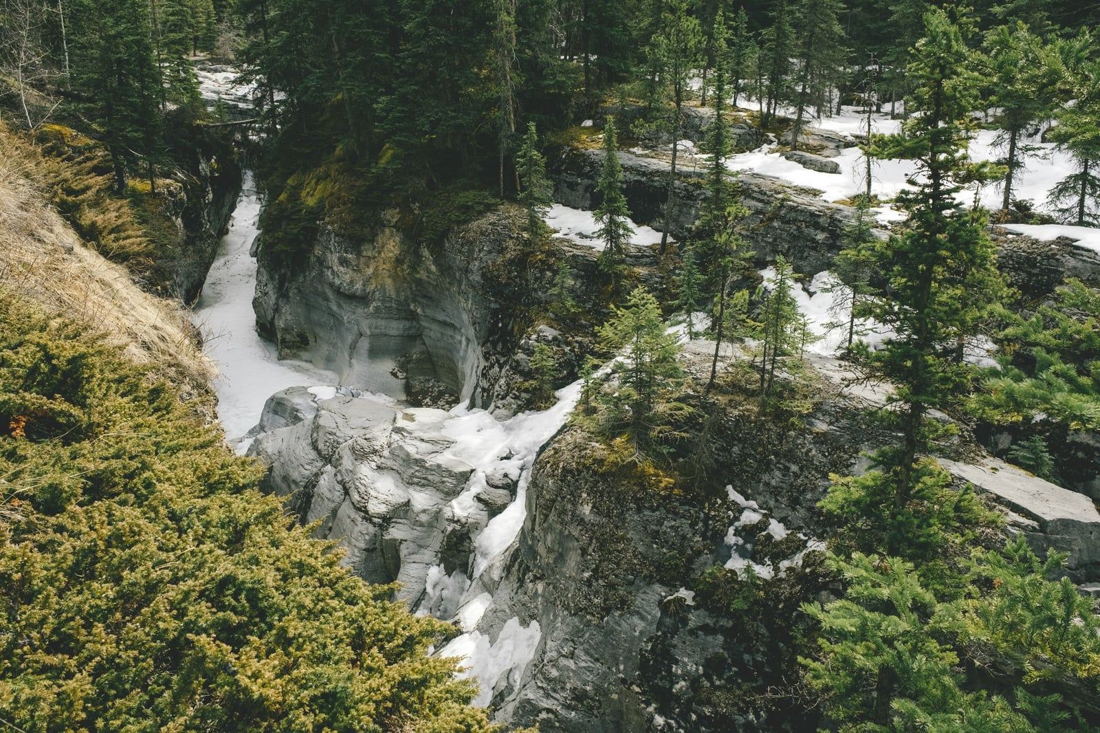 A high-angle view of the deep limestone gorge and footbridge at Maligne Canyon in Jasper National Park dusted with snow among evergreen forest.