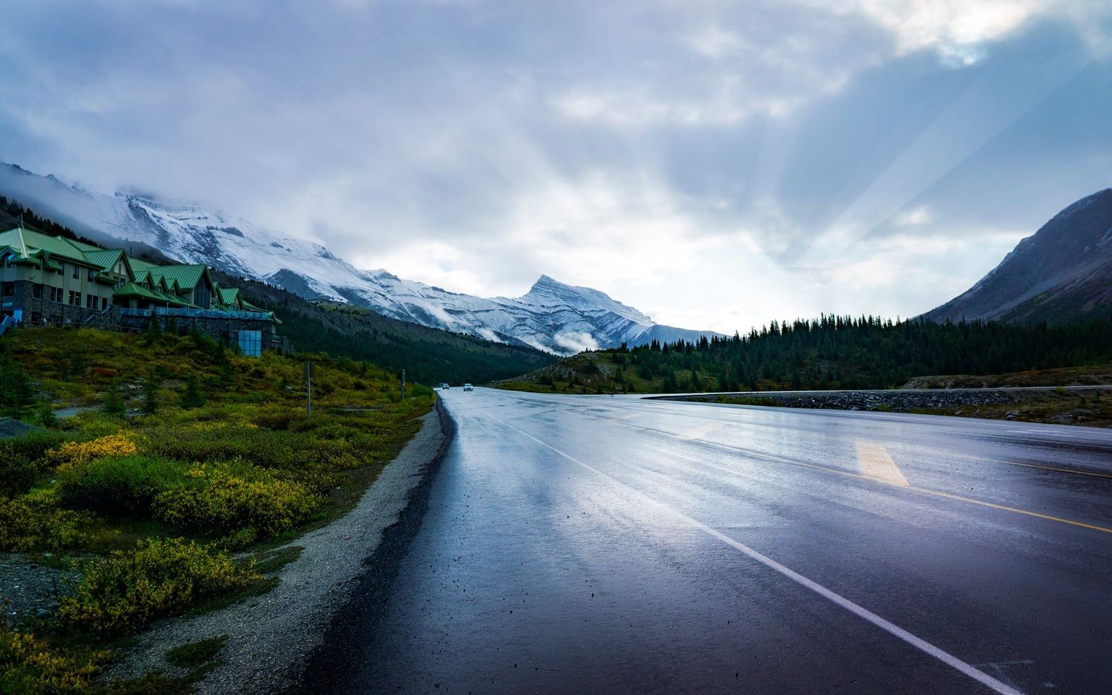 The Icefields Parkway passes the Columbia Icefield Discovery Centre beside autumn-yellow shrubs and snow-dusted mountains in Jasper National Park.