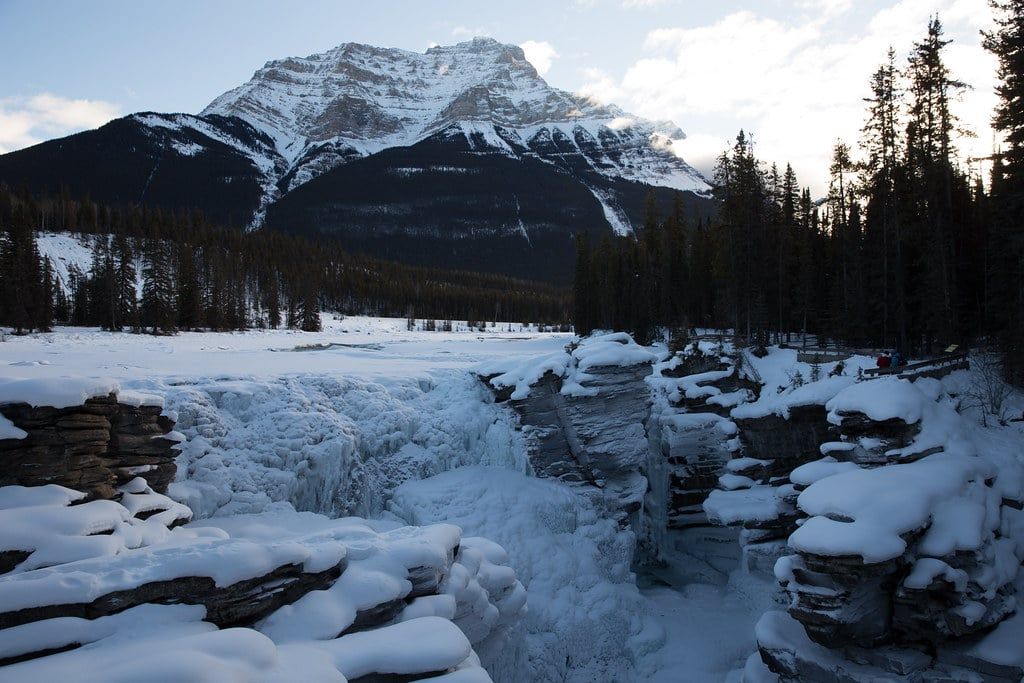 Snow and ice blanket the rocky gorge of frozen Athabasca Falls with Mount Kerkeslin in the background at Jasper National Park.
