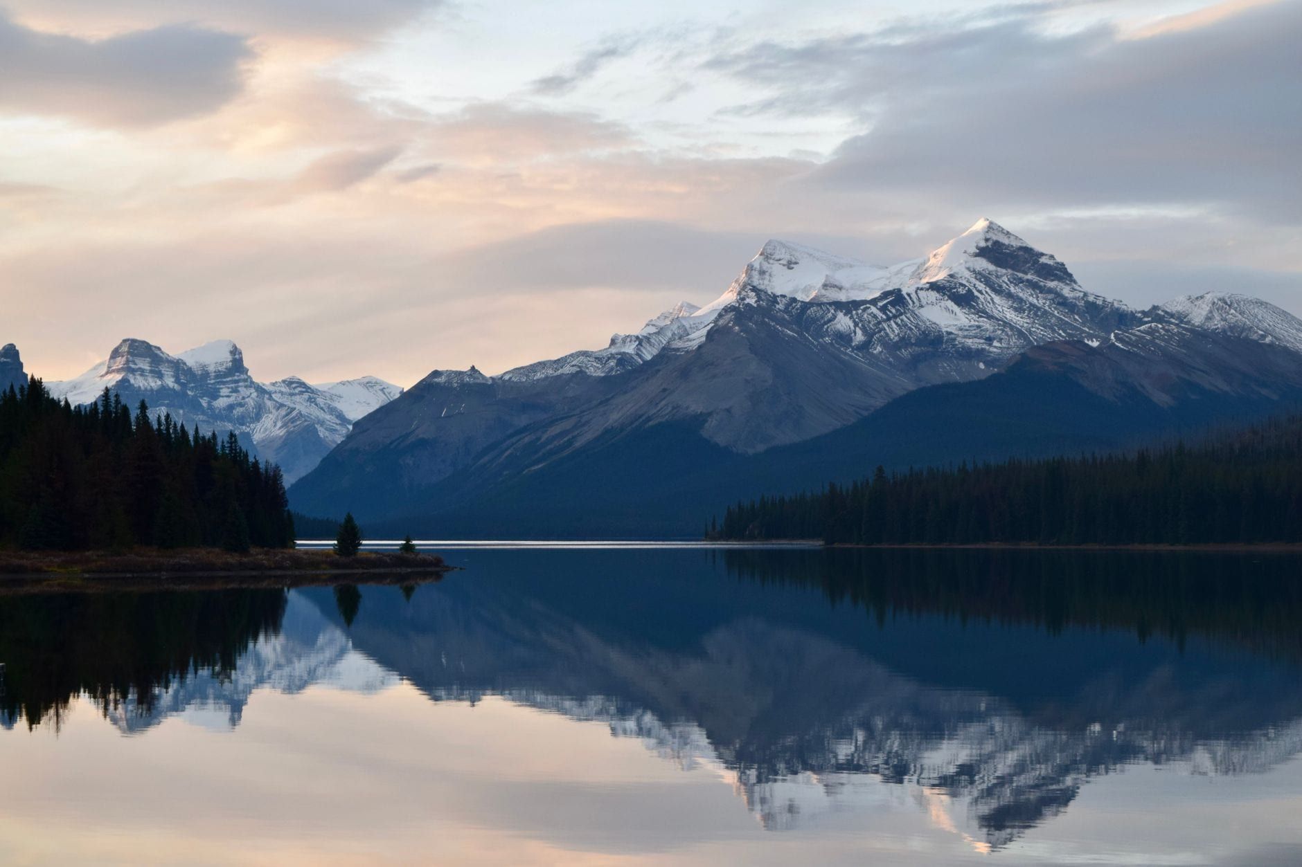 Snow-dusted mountains reflect in the calm waters of Maligne Lake at dawn in Jasper National Park.