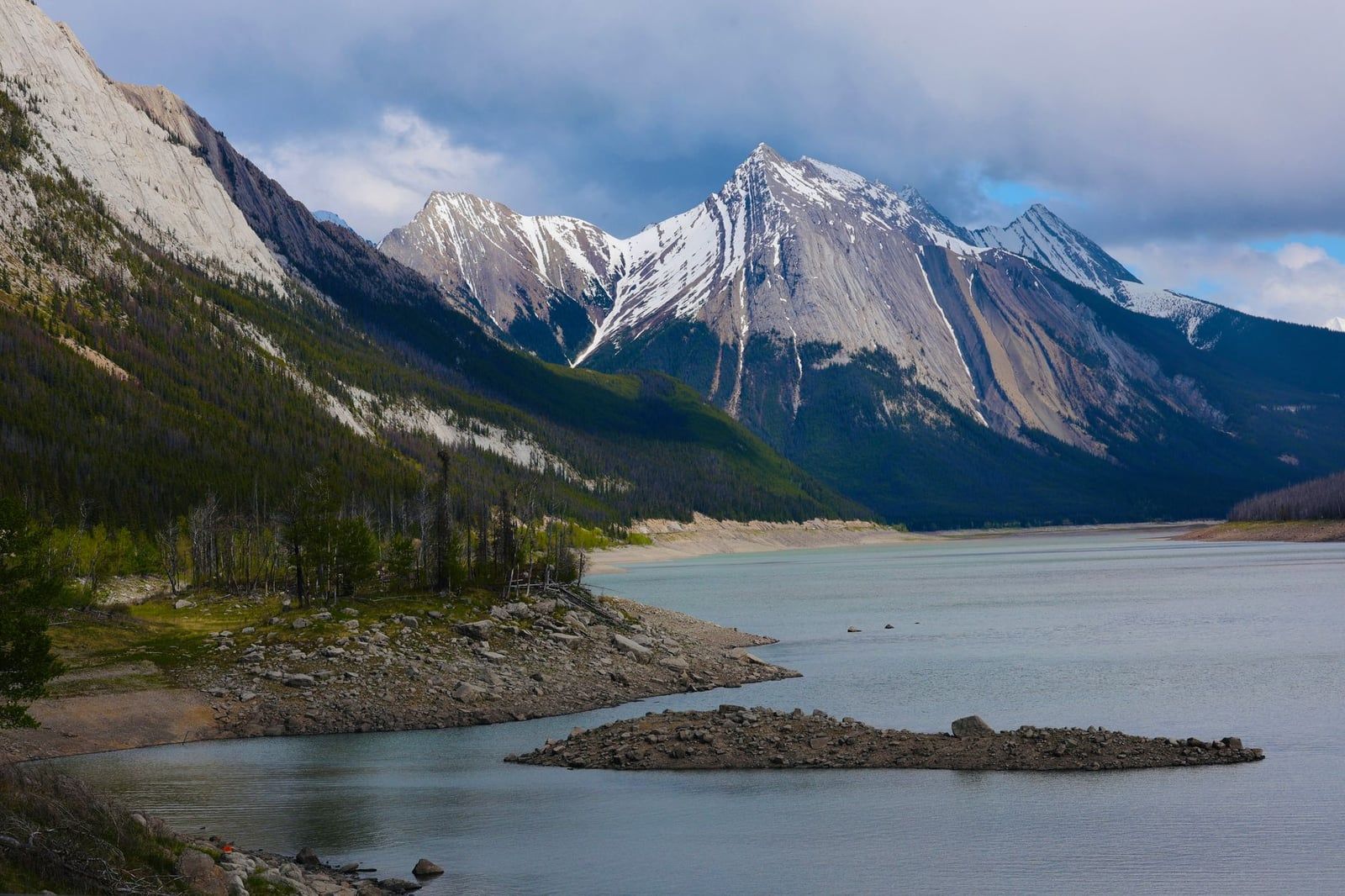El lago Medicine presenta una orilla rocosa expuesta enmarcada por picos montañosos escarpados con nieve en el Parque Nacional Jasper.