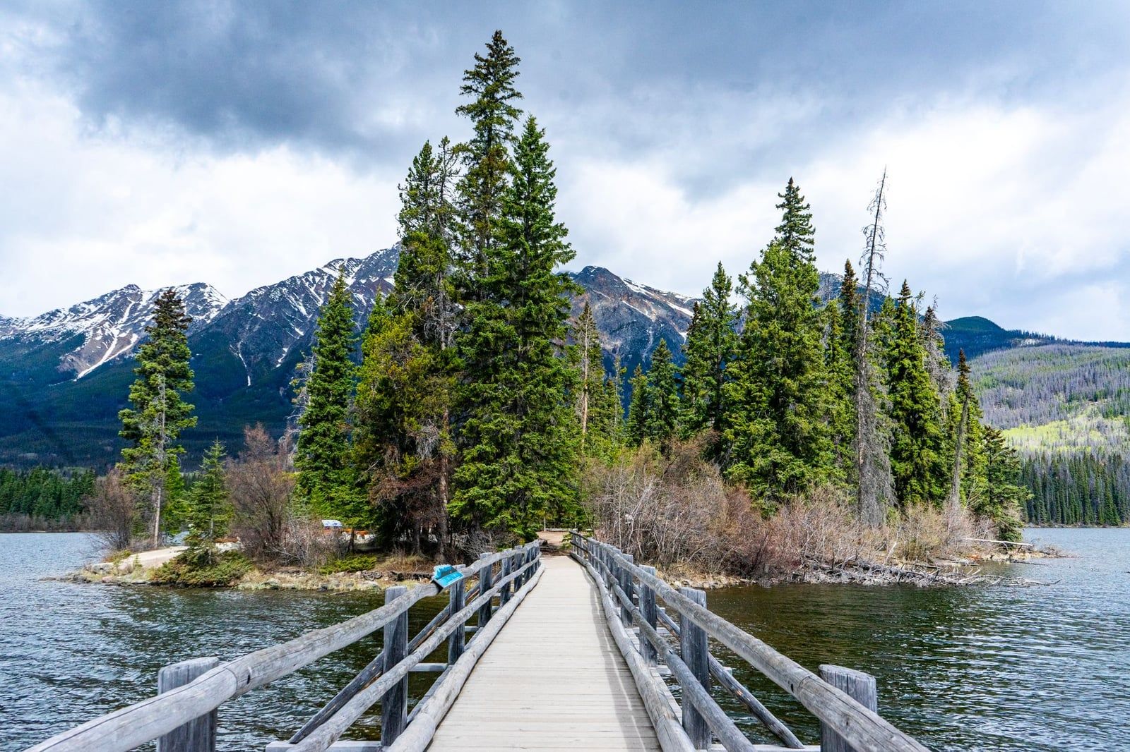 A wooden footbridge leads across the water to the forested Pyramid Island on Pyramid Lake in Jasper National Park.