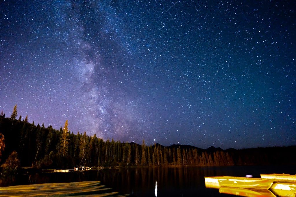 The Milky Way shines in the starry night sky over the forested shore and calm waters of Pyramid Lake in Jasper National Park.