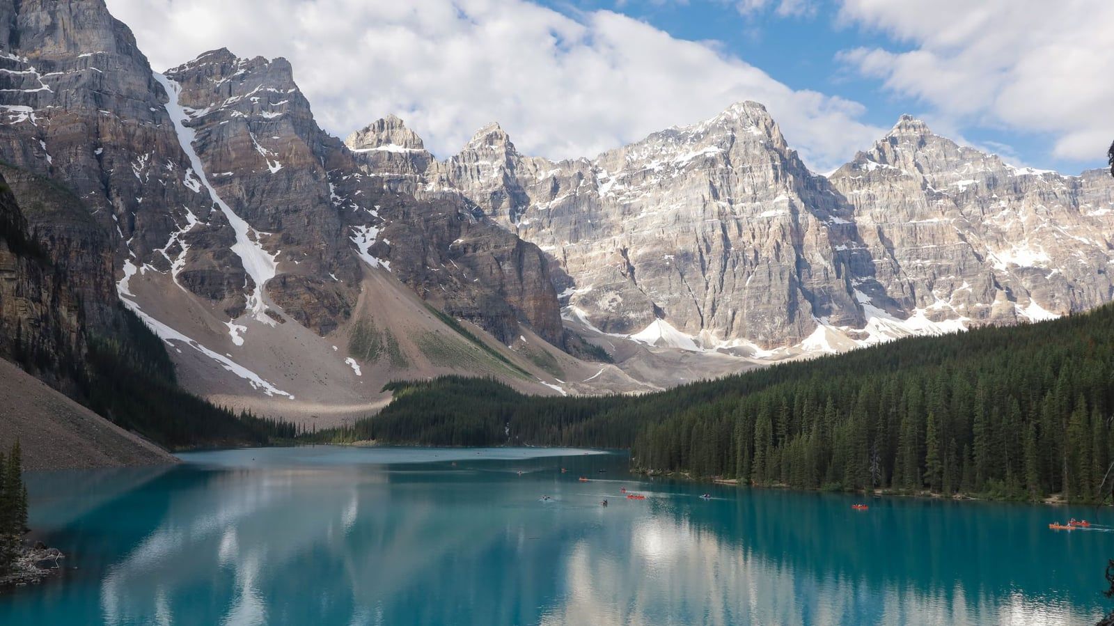 Turquoise waters of Moraine Lake reflect the rugged Valley of the Ten Peaks beneath a partly cloudy sky in Banff National Park.
