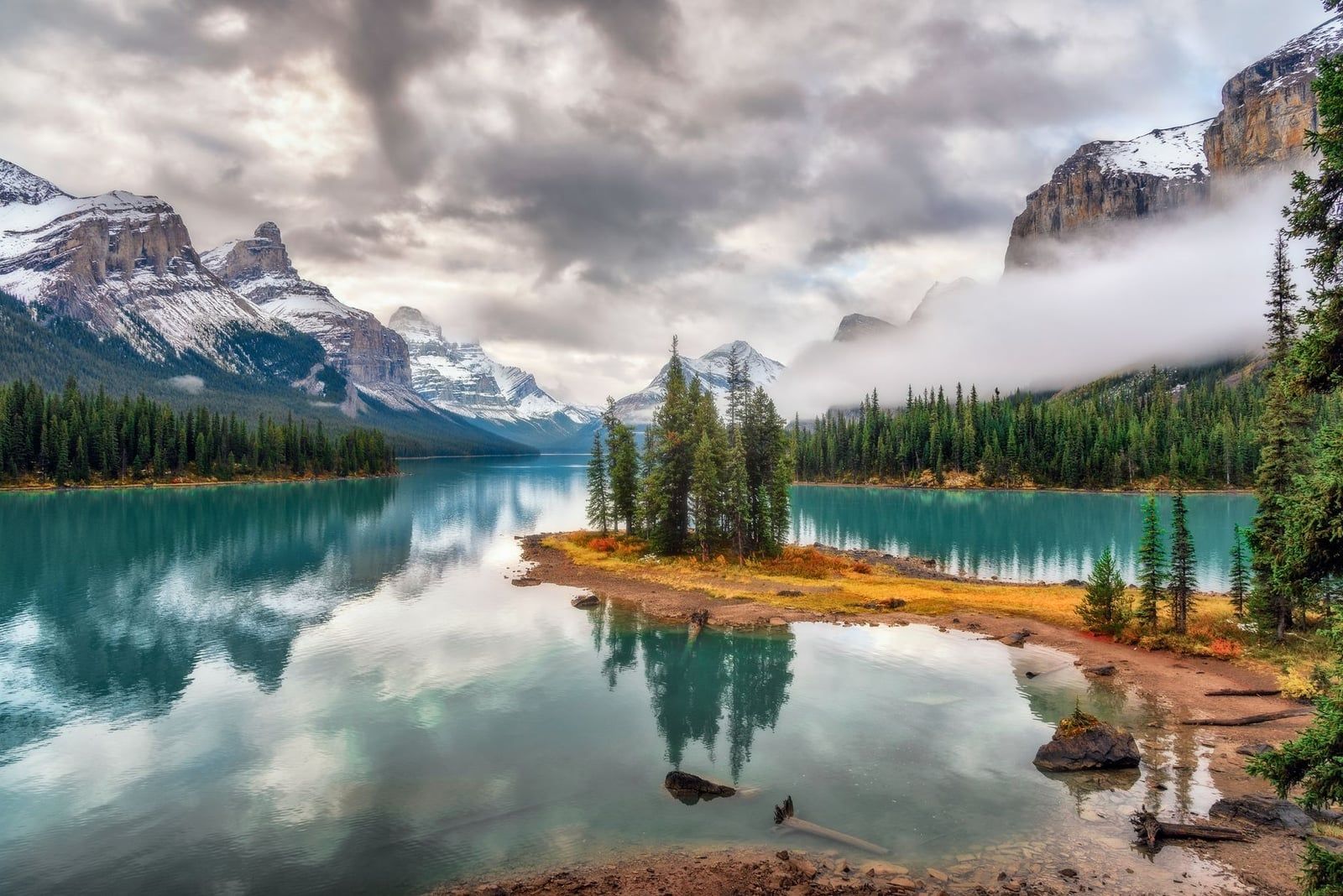 Spirit Island, a small grove of evergreen trees on an islet in turquoise Maligne Lake, framed by snow-dusted mountains in Jasper National Park.