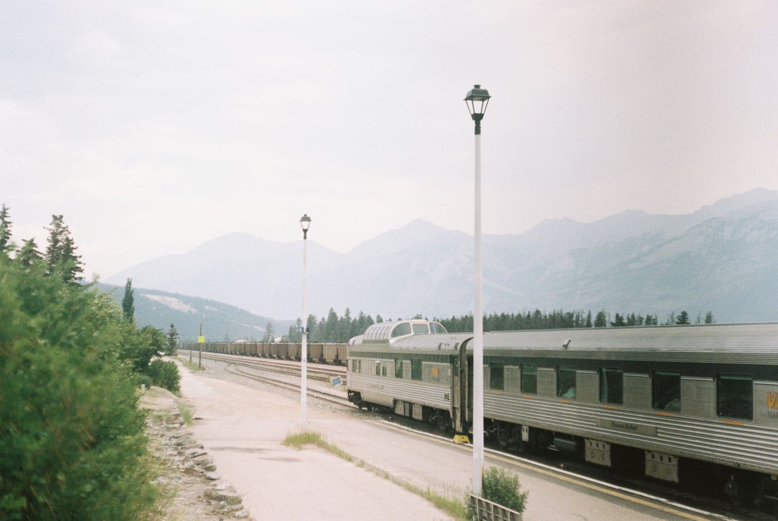 Een passagierstrein staat op het perron van het station van Jasper met de Canadese Rockies op de achtergrond.
